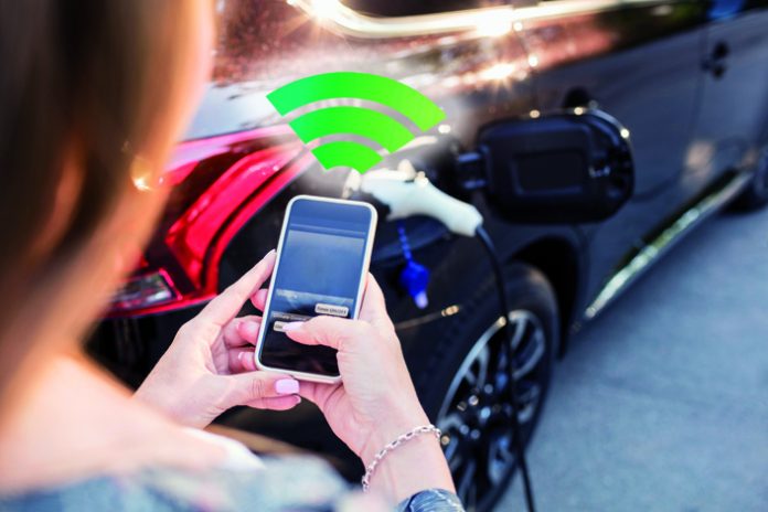 Woman using smart phone while standing by charging electric car